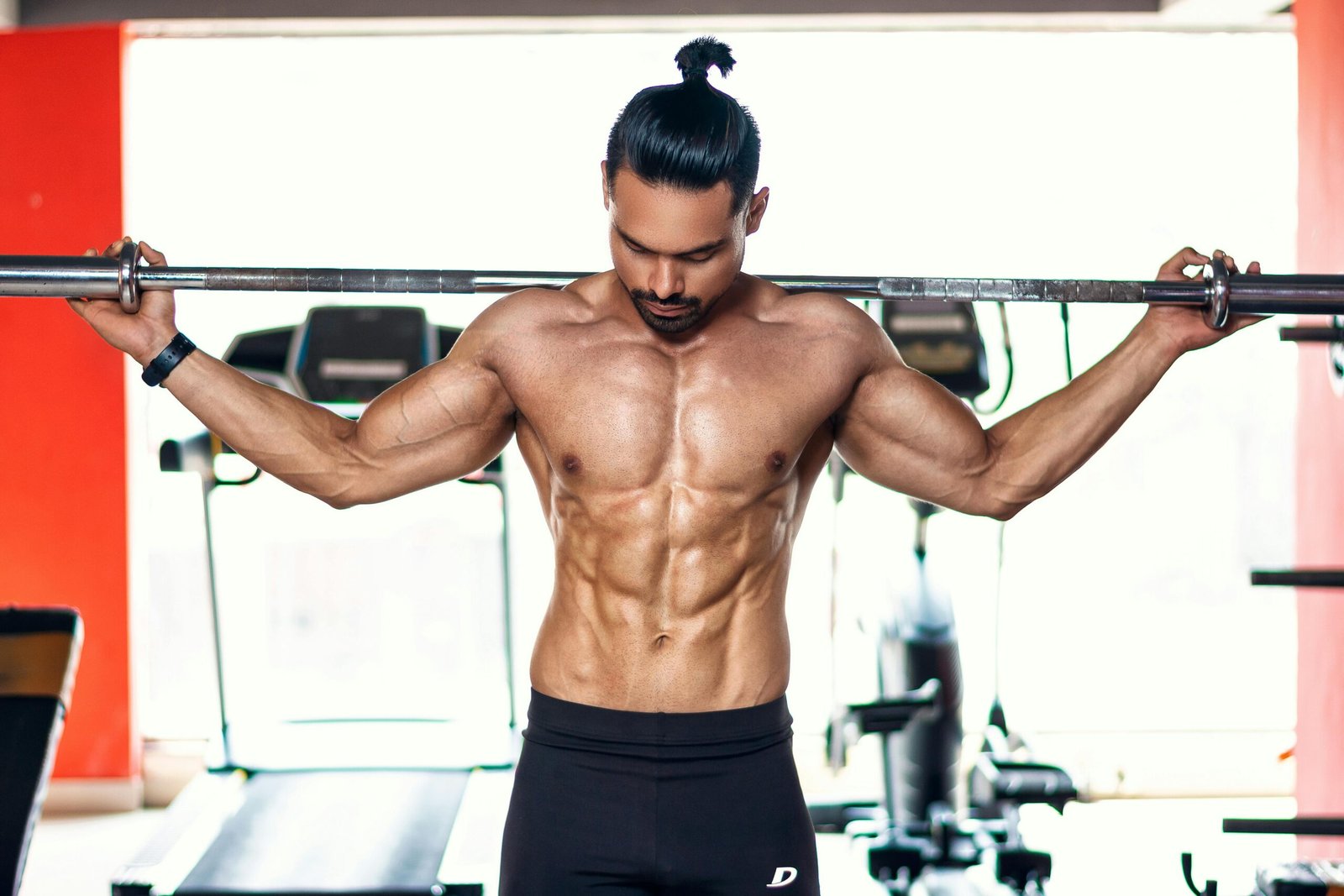 Strong and shirtless man lifting weights indoors in Pune gym.